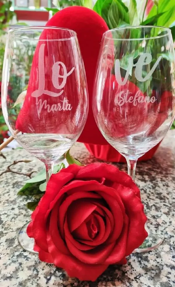 Calici in vetro incisi con il nome di persone su un tavolo con delle rose